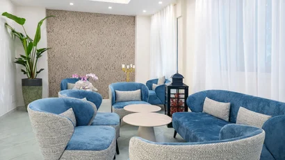 Hotel Regal: comfort ed eleganza a Rimini Sala d'attesa moderna con sedute blu e grigie, tavoli rotondi, pianta e tende leggere.